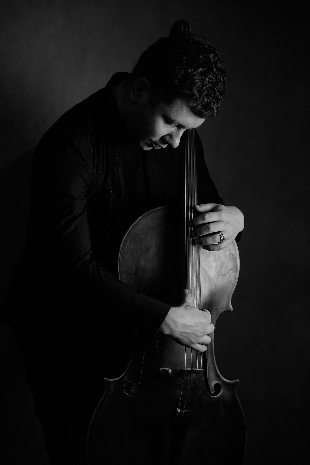 Czarno-biały portret artystyczny mężczyzny z wiolonczelą w klimacie low-key, wykonany w Katowicach na Śląsku przez fotografa Andrzeja Hanzlika.