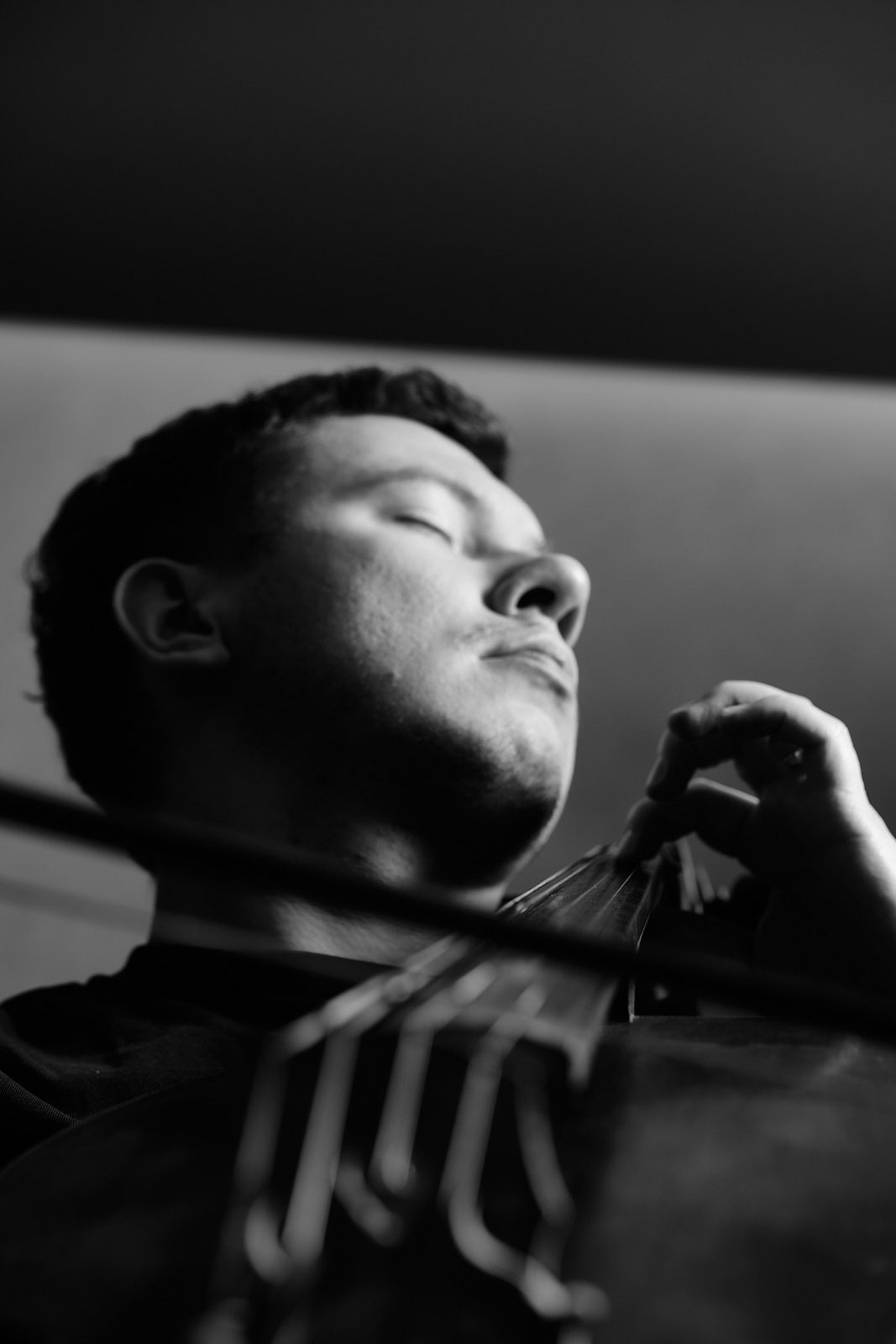 Czarno-białe zdjęcie muzyka z przymkniętymi oczami podczas gry na wiolonczeli, perspektywa z dołu, profesjonalny portret wykonany w Katowicach przez Andrzeja Hanzlika.