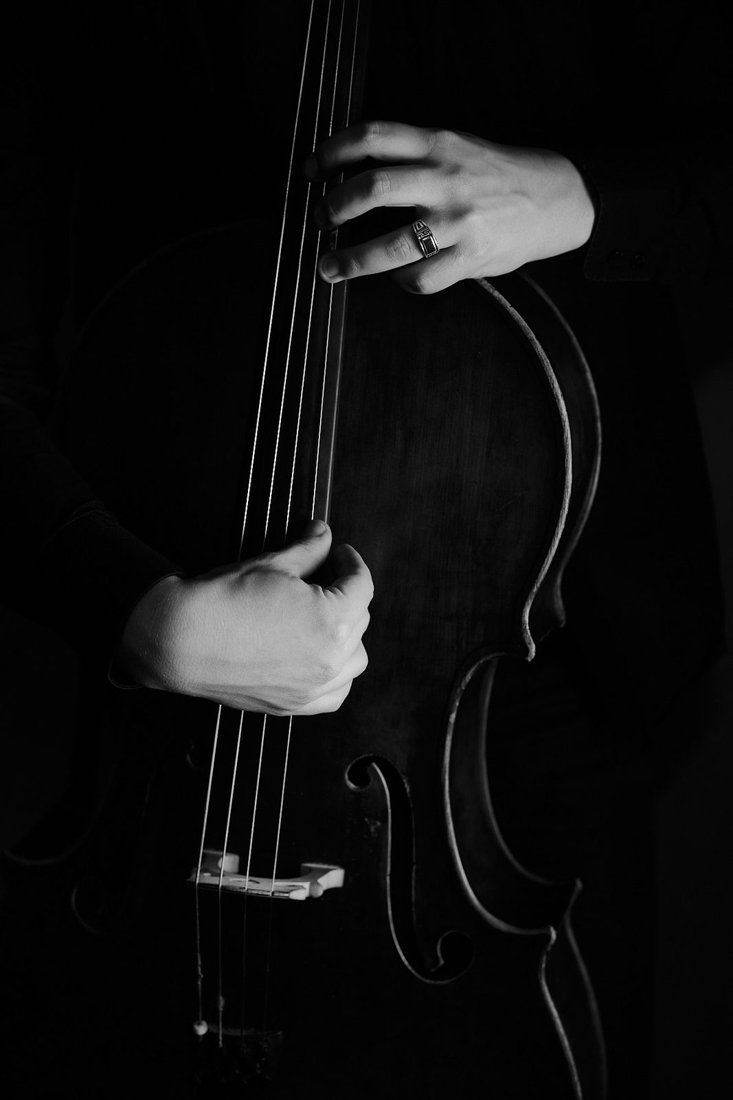 Zbliżenie na dłonie muzyka grającego na wiolonczeli, czarno-biały detal w niskim kluczu oświetleniowym, fot. Andrzej Hanzlik, Katowice.